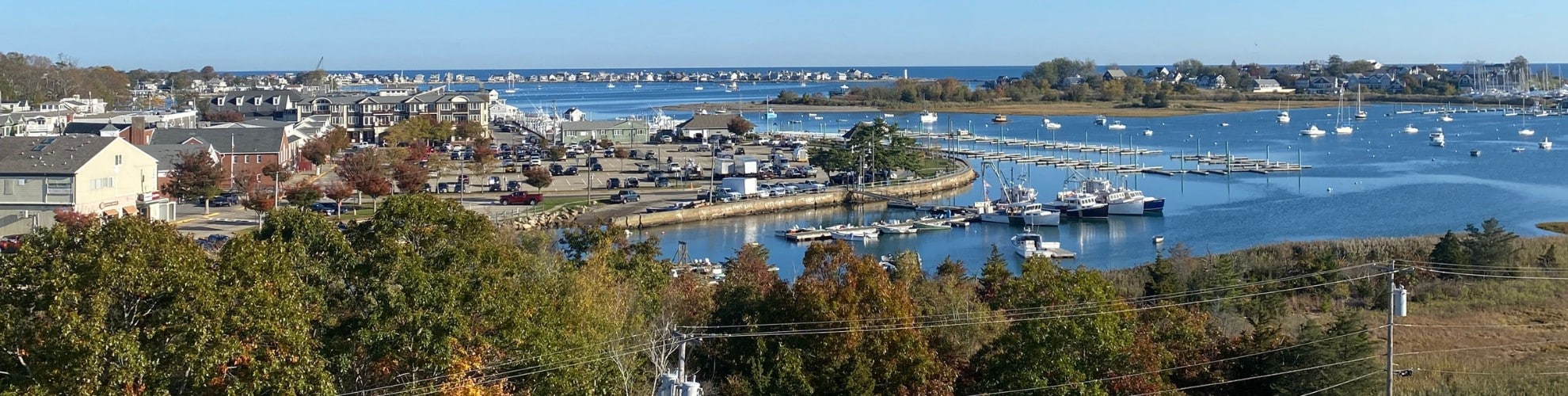 Coastal view showing trees along the shoreline with boats anchored in a South Shore harbor on a clear autumn day.