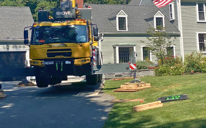 Top Notch Tree crane stationed in a driveway on a property in Plymouth County, MA, using strategic placement to ensure safe and damage-free tree removal.