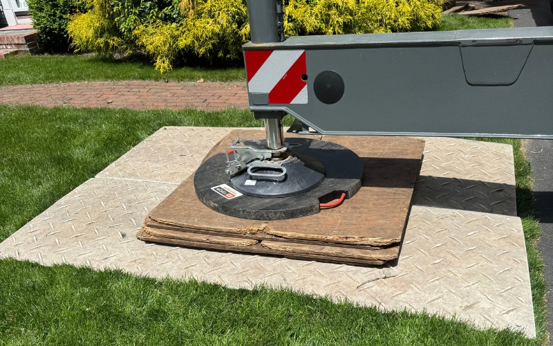 Crane outrigger set up on lush green grass with layers of AlturnaMATS, plywood, and a DICA pad to prevent sinking and protect the lawn.