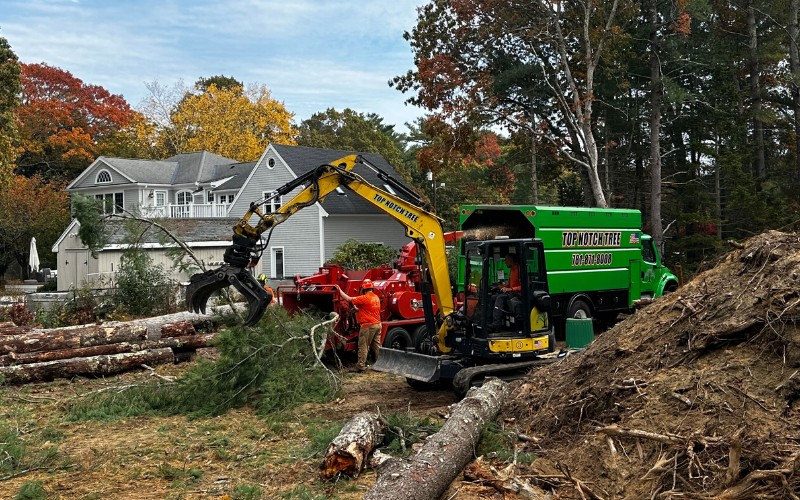 Multiple pieces of Top Notch Tree equipment, including an excavator and wood chipper, are working together on a large residential lot clearing project with crew members coordinating the operation
