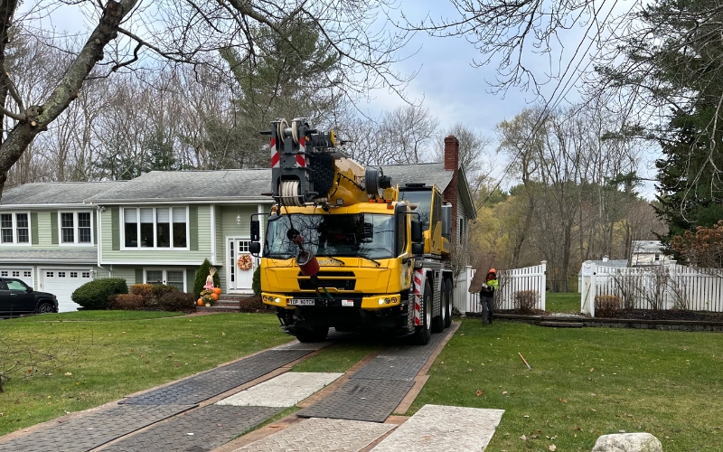 A tree removal crane truck using ground protection mats on a residential driveway during tree removal to prevent property damage.