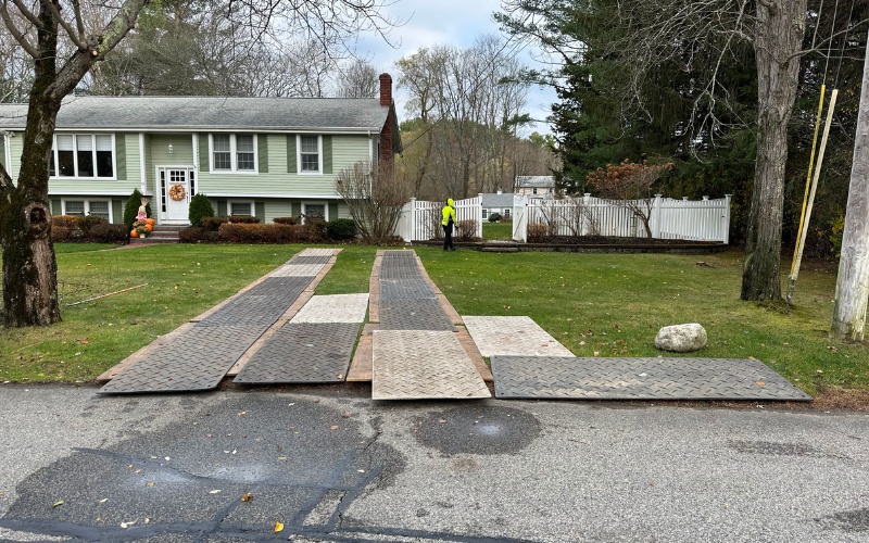 Wood protection mats are laid across a residential driveway to prevent damage during tree removal equipment access.