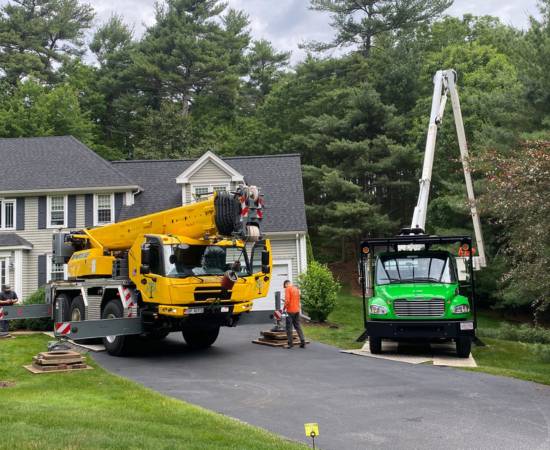 A yellow truck and green bucket truck owned by Top Notch Tree parked in front of a client's home for tree pruning and trimming.